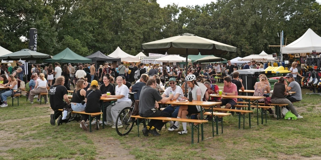 Menschen auf Bierbänken, die ihr Essen beim Veganmania Streetfood Festival genießen.