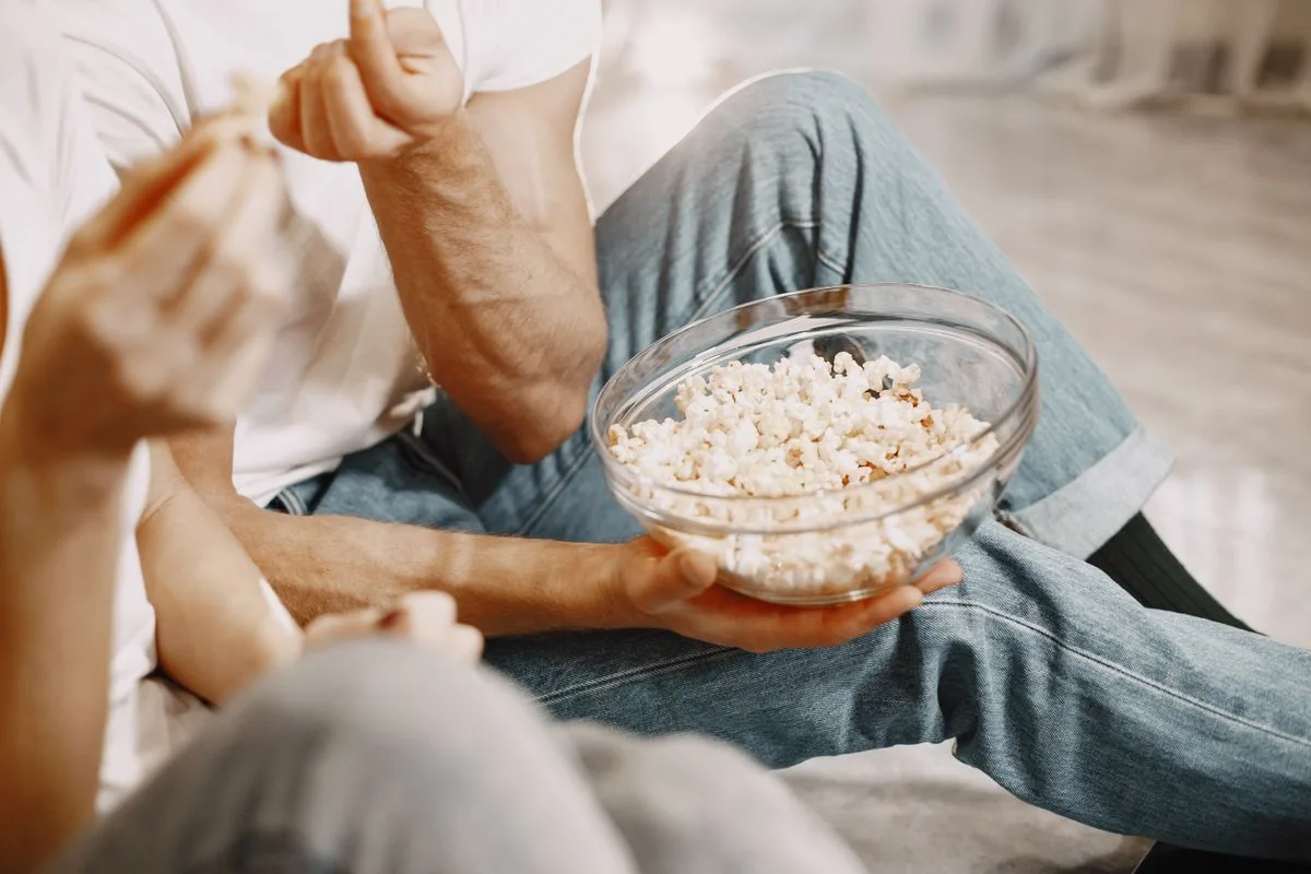zwei Personen sitzen nebeneinander und essen Popcorn aus einer Glasschüssel