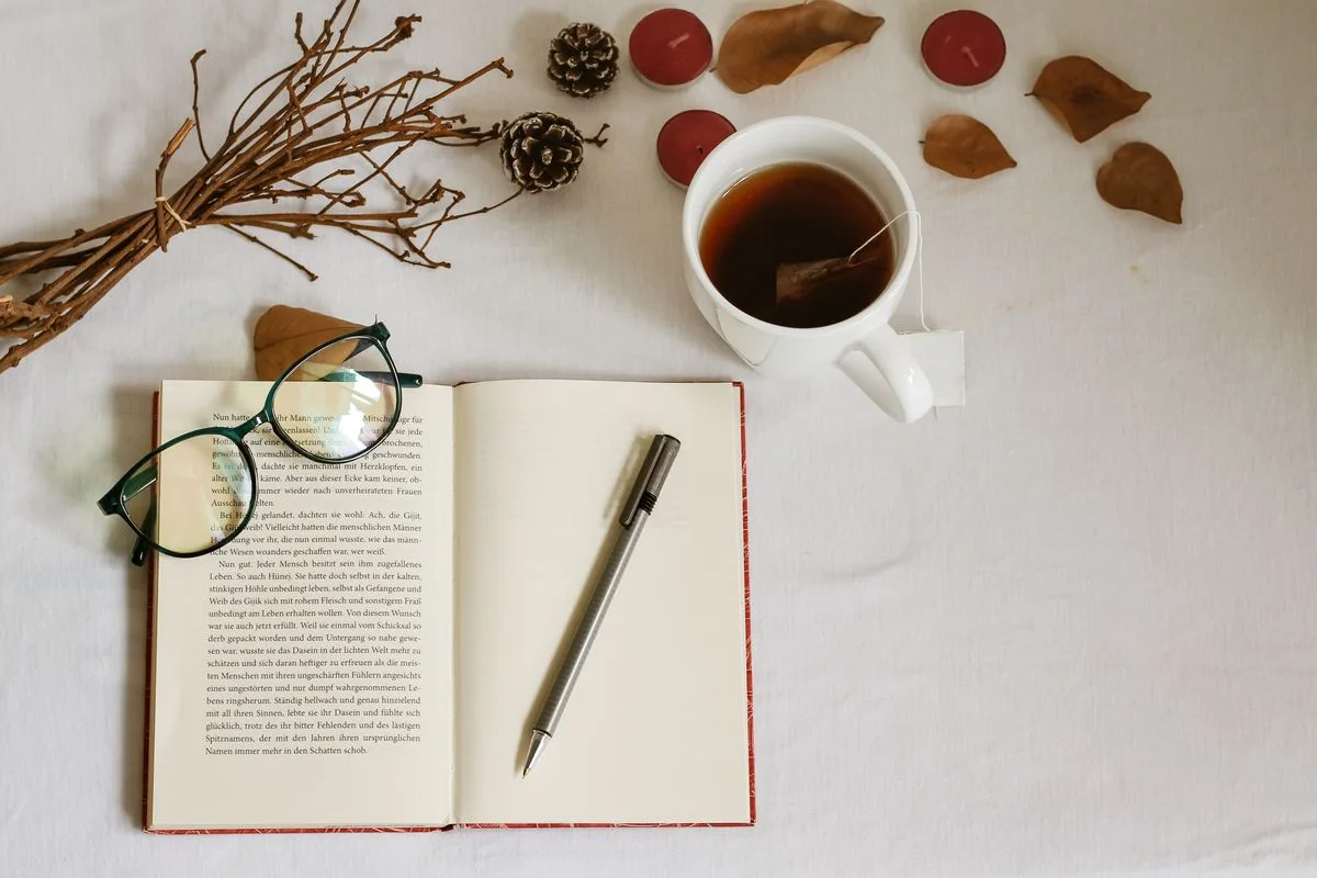 Aufgeschlagenes Buch, Tee und herbstliche Blätter liegen auf einem Tisch
