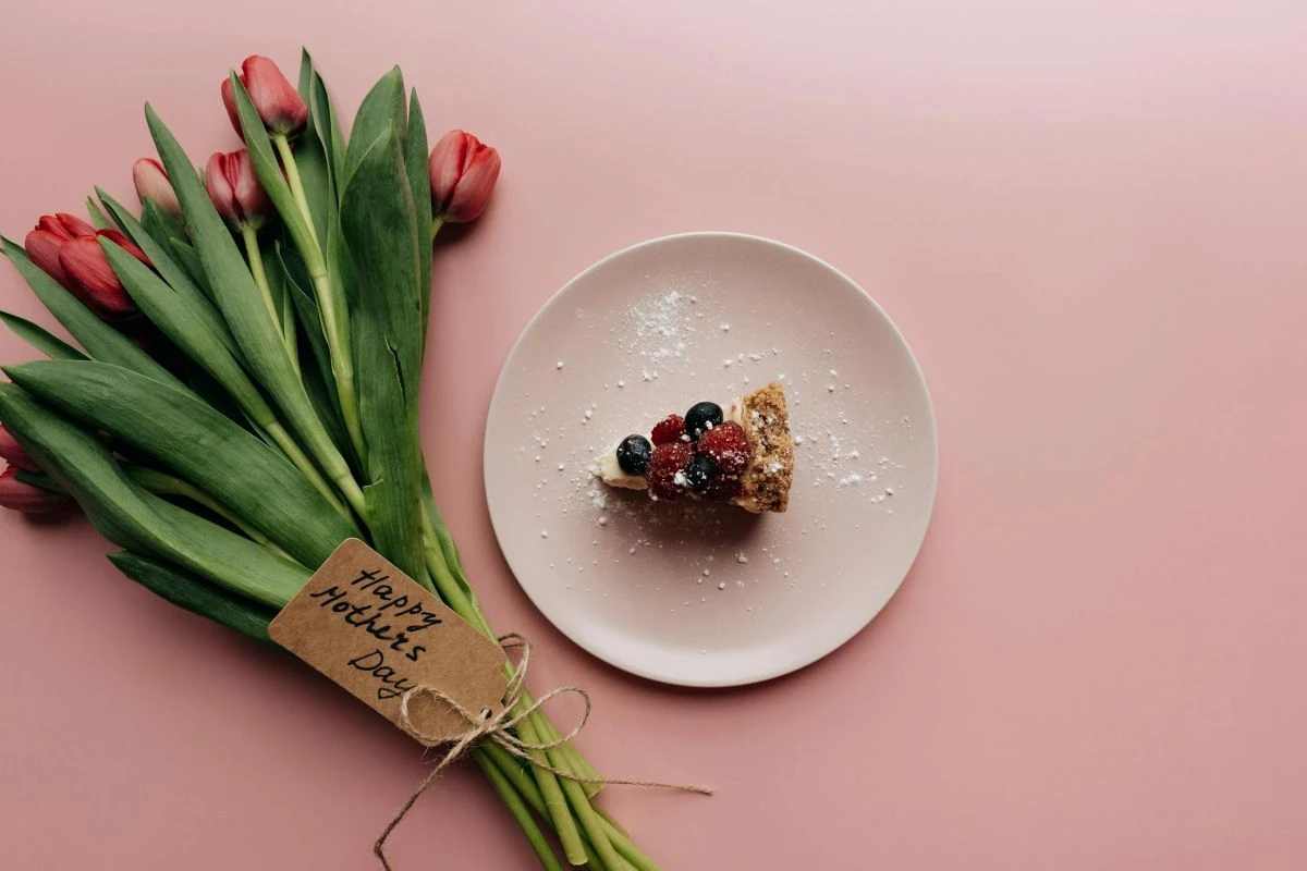 Tulpenstrauß mit einem Schild "Happy Mother's Day" und ein Teller mit einem Kuchenstück