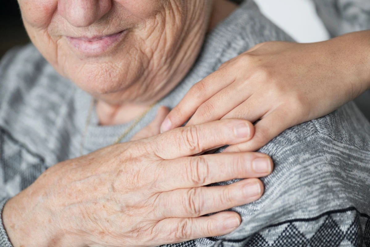 Ältere Person, die ihre Hand zärtlich auf die Hand einer jüngeren Person auf ihrer Schulter legt