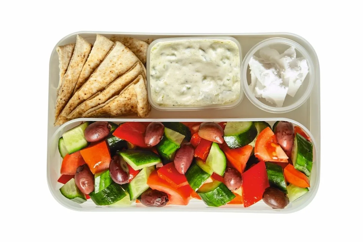 Jausenbox mit verschiedenen Fächern mit Tomate-Gurke-Oliven-Salat, veganem Feta, Joghurtsauce und Pitastücken