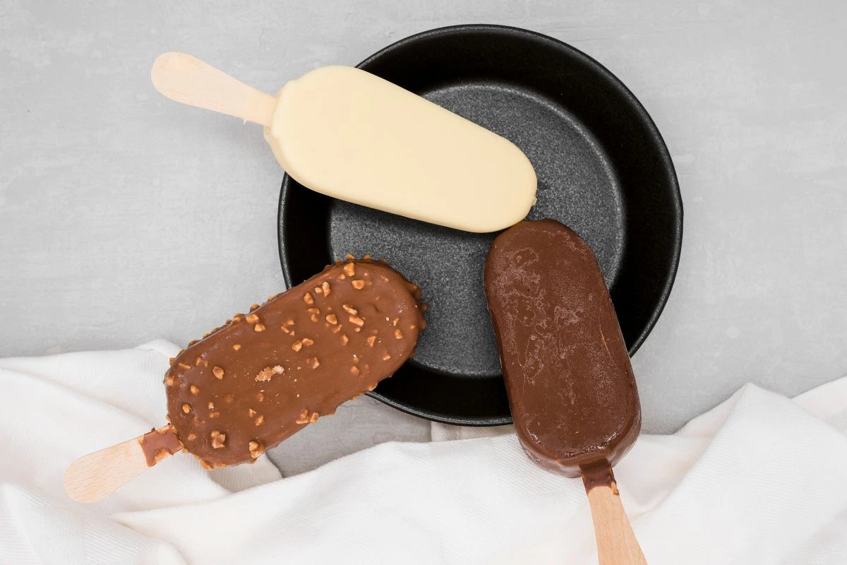 Drei Schokoladen-Eis am Stiel auf einem schwarzen Teller.