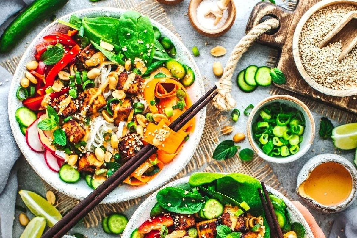 Bowl mit Reisnudelbasis, darauf Karotten, Radieschen, Gurken, Tomaten, Erdnüsse und Sesam